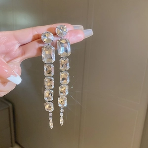 Close-up of sparkling long tassel earrings with silver rectangle and drop-shaped crystals