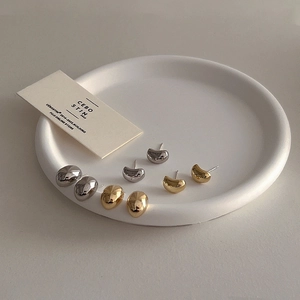 Detail of minimalist gold and silver bean stud earrings on a white ceramic tray