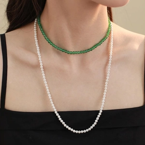 Detail of layered jewelry featuring a green agate bead choker and long pearl necklace