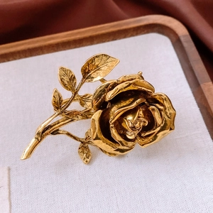 Detailed close-up of a vintage golden rose brooch with intricate petals and textured leaves