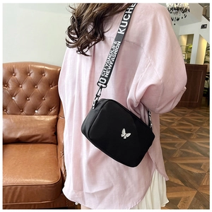 Close-up of black nylon crossbody bag with silver butterfly and lettered strap