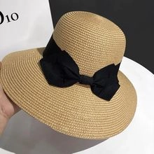 Detail of hand holding a wide brim straw sun hat with a decorative black ribbon bow