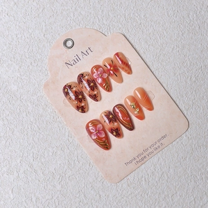 Detailed view of handmade almond fake nails with floral relief and golden metallic lines