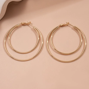 Detail view of double layer gold geometric hoop earrings on a light pink background