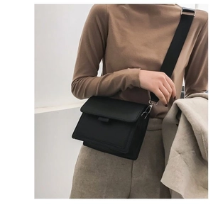 Classic black square crossbody bag with wide shoulder strap worn by a female model