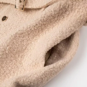 Detail of curly lamb wool coat featuring golden metal buckle and polished round button