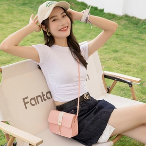 Pink crossbody bag with pearl charm and white strap detail on green lawn background