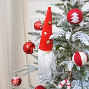 Plush Christmas gnome ornament with red hat and gold star hanging on snowy tree