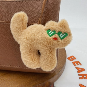 Detail of cream plush cat pendant with green heart sunglasses on a brown leather bag