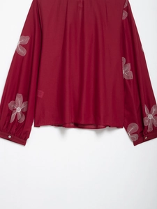 Close-up of white floral embroidery on long sleeves of raspberry red vintage blouse
