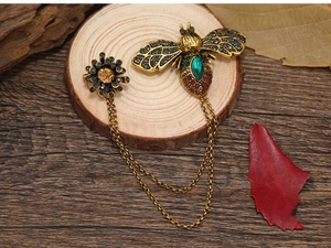 Detailed close-up of a vintage bee brooch with green gemstone and antique gold chains