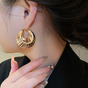 Close-up of chunky gold hoop earrings with intricate diamond texture on the metal surface