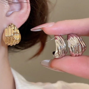Detailed close-up of textured gold and silver metal earrings with unique wrinkled design