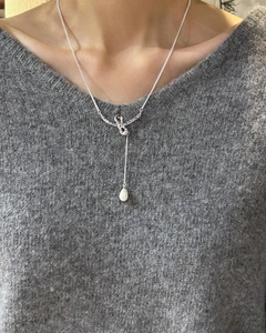 Detail of sterling silver necklace featuring a bow pendant and teardrop pearl on a model