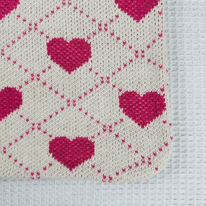 Close-up of heart-patterned knitted fabric texture in beige and pink colors