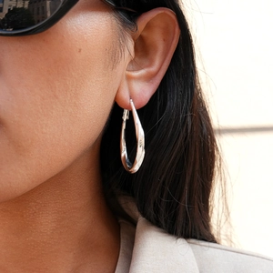 Macro side view of model wearing a twisted silver drop earring with polished finish