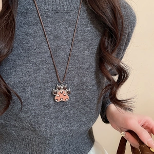 Detail of pink leopard print paw pendant on brown braided cord worn on a grey sweater