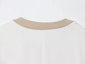 Detailed close-up of contrasting round neckline and flat stitching on white knit top