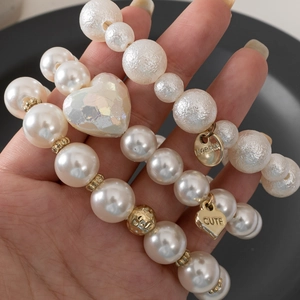 Close-up of three pearl bracelets with heart charms and gold beads held in hand