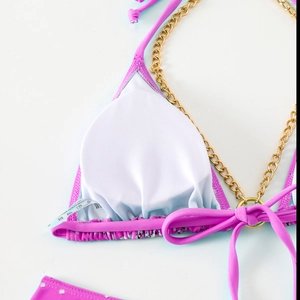 Detail of pink bikini top with gold metal chains, white lining and laundry care label