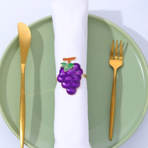 Detailed view of a purple grape napkin ring with green leaves on a white cloth napkin