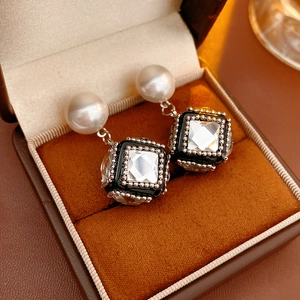 Close-up of geometric cube earrings with white pearls and sparkling zircon inlays