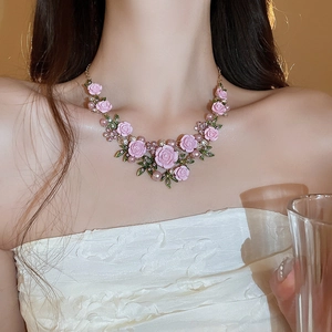 Detail of pink resin rose necklace with green leaves, pearls and rhinestones on neck