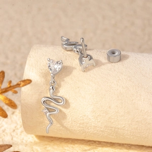 Boucles d'oreilles serpent en argent avec clous coeur en zircone sur support beige