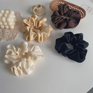 Flat lay of four satin hair scrunchies in cream, gold, brown and black with stylish props