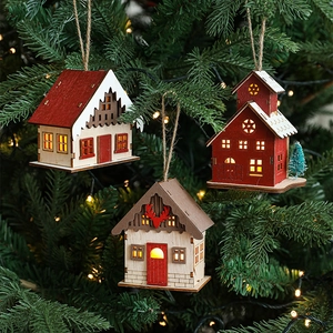 Lighted wooden Christmas house ornaments hanging on a festive tree branch with warm LED light