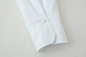 Close-up of white long sleeve shirt cuff with matching fabric button and fine stitching