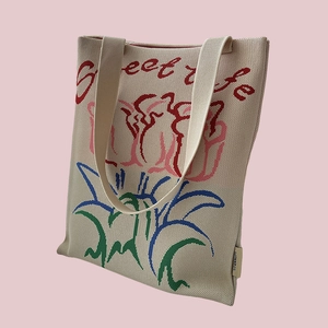 Detailed close-up of beige knitted tote bag with colorful floral embroidery and text