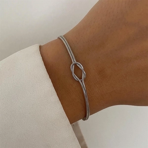 Minimalist silver stainless steel knotted cuff bracelet shown on wrist with elegant sleeve