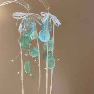 Detail von Muschel-Quastenohrringen mit grünen Blütenblättern und weißen Schleifen