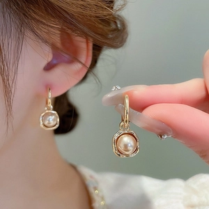 Détail de boucles d'oreilles carrées en perle dorée avec papillon en zircon