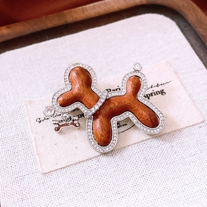 Detail of zircon-studded wooden balloon dog brooch with small hanging bone charm