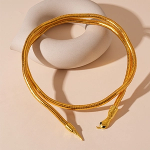 Elegant gold snake necklace with scale texture and black stone eyes on a minimalist stand