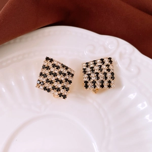 Detail shot of square checkerboard gold stud earrings on an elegant ceramic plate