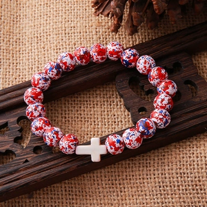 Detail of beaded bracelet with red, white and blue stones and a white cross charm
