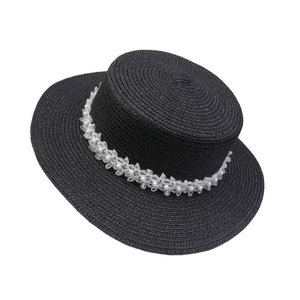 Detail of black straw hat featuring white lace flowers and pearl embellishments on brim