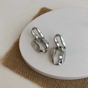 Close-up of modern irregular silver chain link earrings on a white minimalist tray