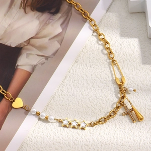 Detail of 18K gold-plated necklace with star, heart and cross charms on a white surface