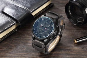 Military-style quartz watch with blue face, leather strap, and calendar on wooden surface