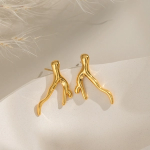 Détail de boucles d'oreilles dorées en forme de branche de corail sur papier beige