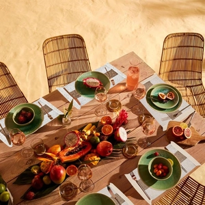 Linen placemat on a wooden table set with tropical fruits and green ceramic dinnerware