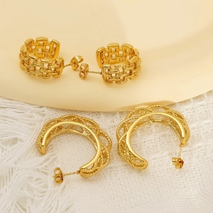 Golden hollow C-shaped earrings with woven mesh and twisted rope texture on a beige plate