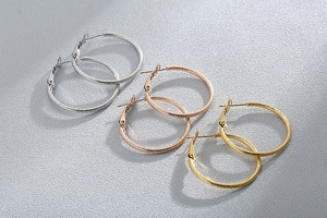 Three pairs of twisted hoop earrings in silver, rose gold, and gold on gray background