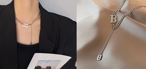 Detail of silver titanium steel Y-necklace with B-letter pendants on silk background