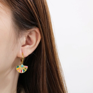 Detailed close-up of fan-shaped enamel earrings with turquoise bead on a model