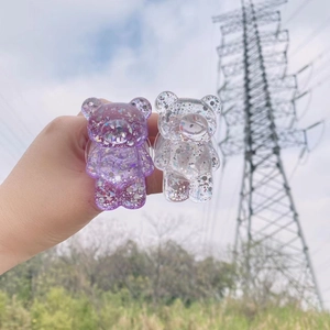 Purple and clear glitter bear phone sockets held against a bright blue sky background